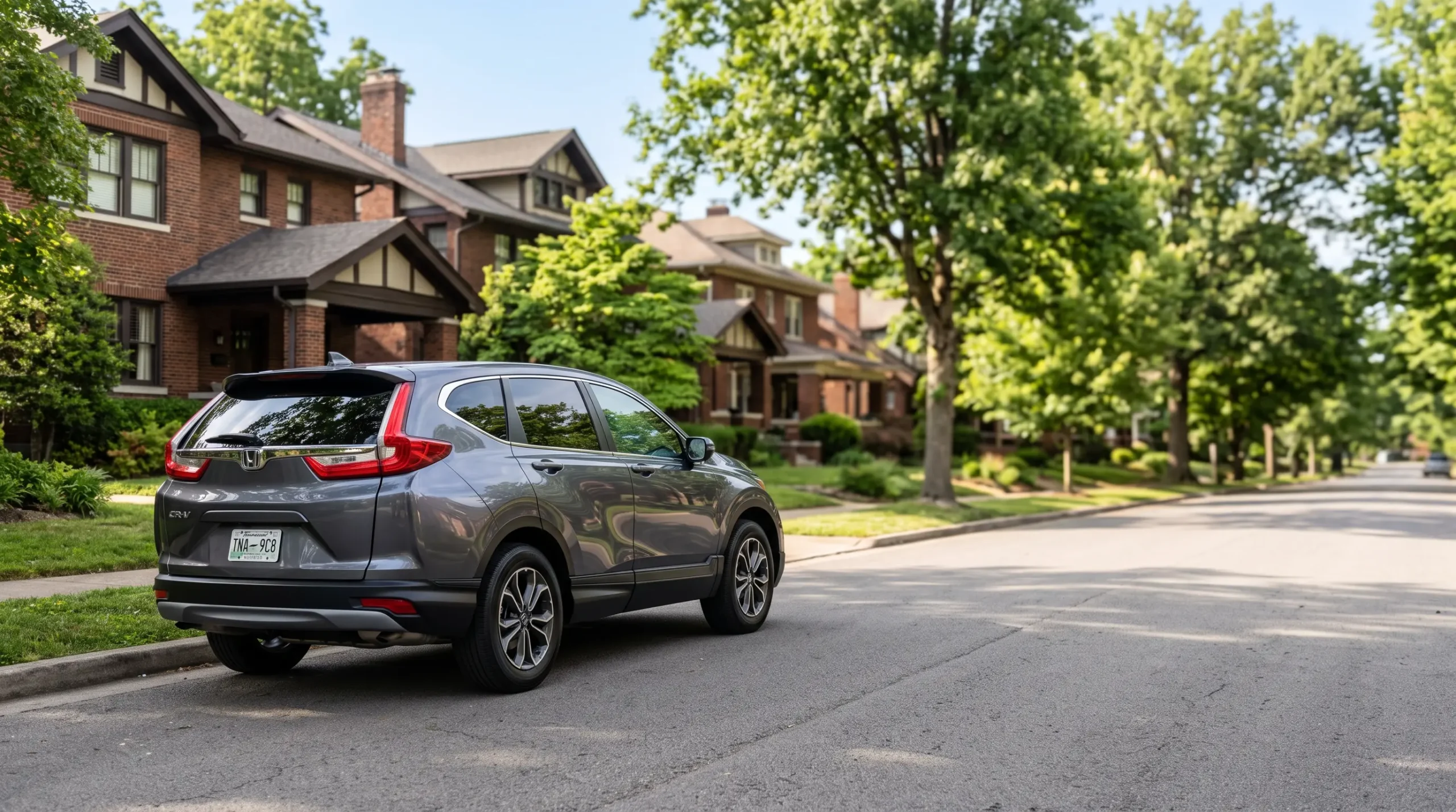 A gray SUV parked along a quiet residential street lined with trees and brick houses.